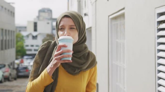 戴着头巾的女人在街上散步，喝着外卖咖啡