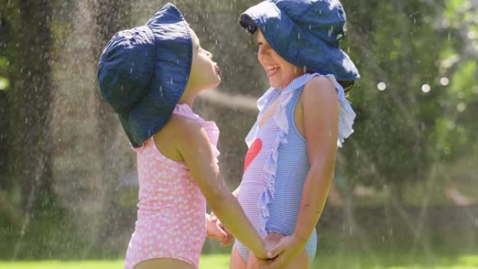 两个小女孩在花园里玩水，两个女孩奔跑，淋湿并大笑。