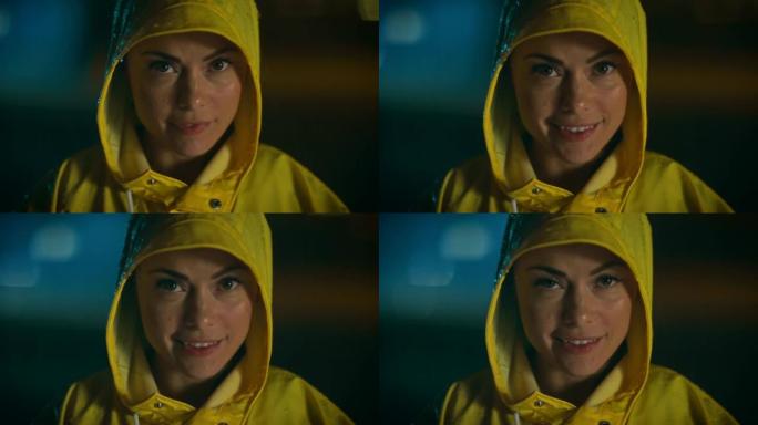 穿着黄色雨衣的棕色眼睛的美丽年轻女孩对着镜头微笑。天气多雨，现在是晚上。