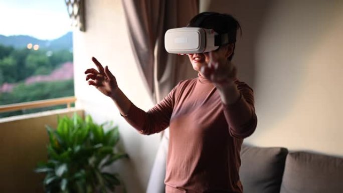 一名亚洲中国中年妇女在客厅使用虚拟现实谷歌在线玩游戏享受虚拟现实