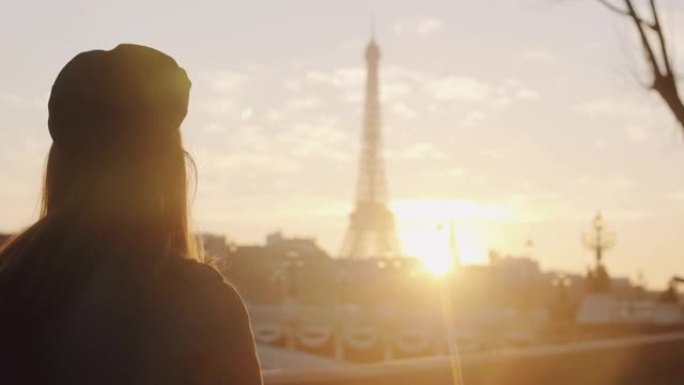 在巴黎慢动作中，快乐的旅游女人沿着埃菲尔铁塔和粉红色天空的日落景色行走的电影后视图。
