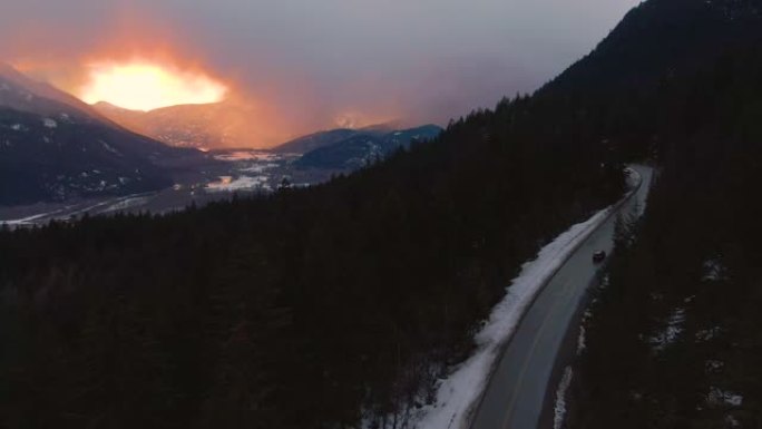 空中: 冬季早晨的天空横跨在加拿大森林中行驶的汽车上方。