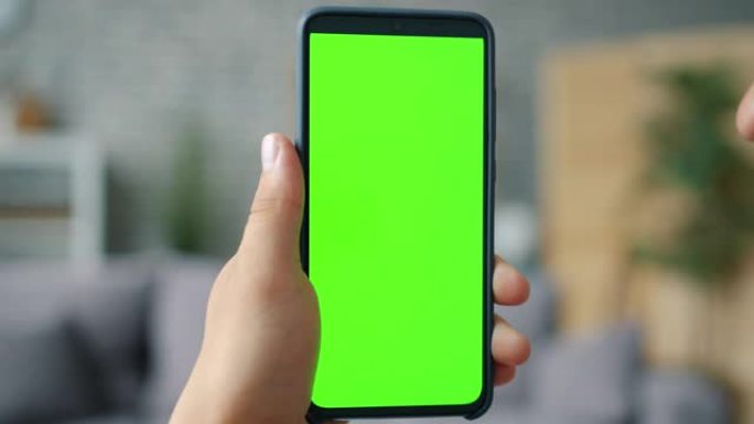 公寓中男性手持色度键绿屏智能手机的特写