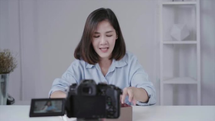快乐美丽的亚洲女人打开品牌或她的订阅者的礼物。女性博客作者从摄像机录制视频以播放拆箱视频。