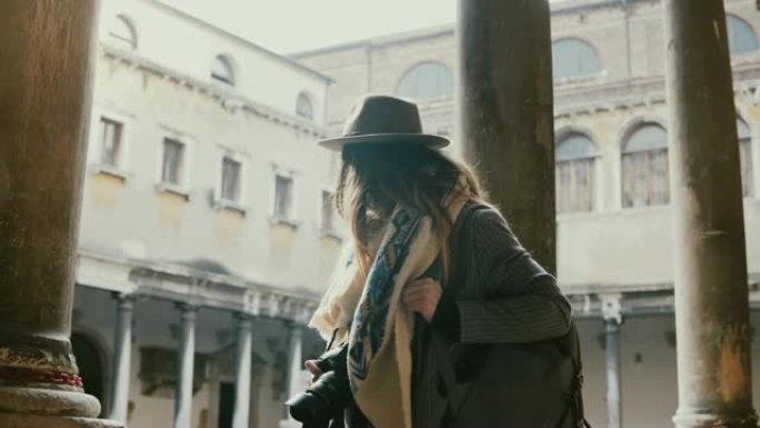 美丽的女性专业摄影师用相机在威尼斯老城的古建筑柱子上拍照。