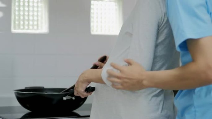年轻的已婚夫妇拥抱站在厨房的桌子旁。丈夫拥抱怀孕的妻子，把手放在她的大肚子上，女人正在准备早餐。生活