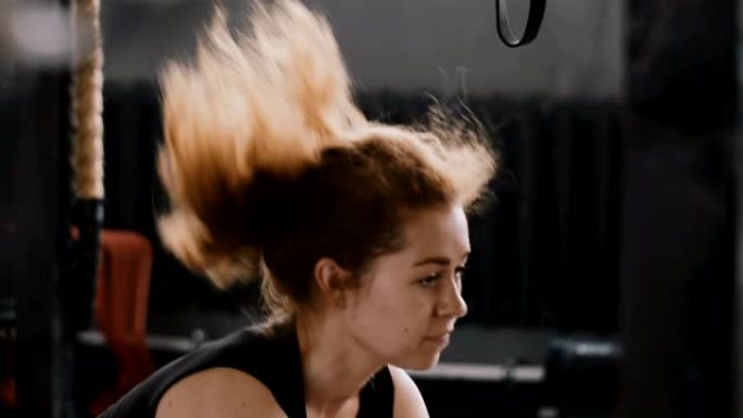 特写慢动作年轻美丽的运动红发女人在大型健身房用战斗绳锻炼，健康的生活方式
