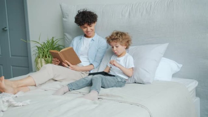 年轻女子和小男孩在床上使用平板电脑微笑着一起享受小工具
