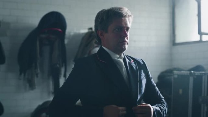 年轻男性马术大师的电影慢动作正在穿着专业服装，然后开始在骑马大厅练习赛马和盛装舞步比赛的练习