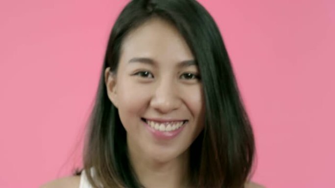 年轻美丽时尚的亚洲女性在粉色背景下用化妆刷在休闲服装上涂抹粉妆。快乐微笑可爱的快乐女人快乐成功。