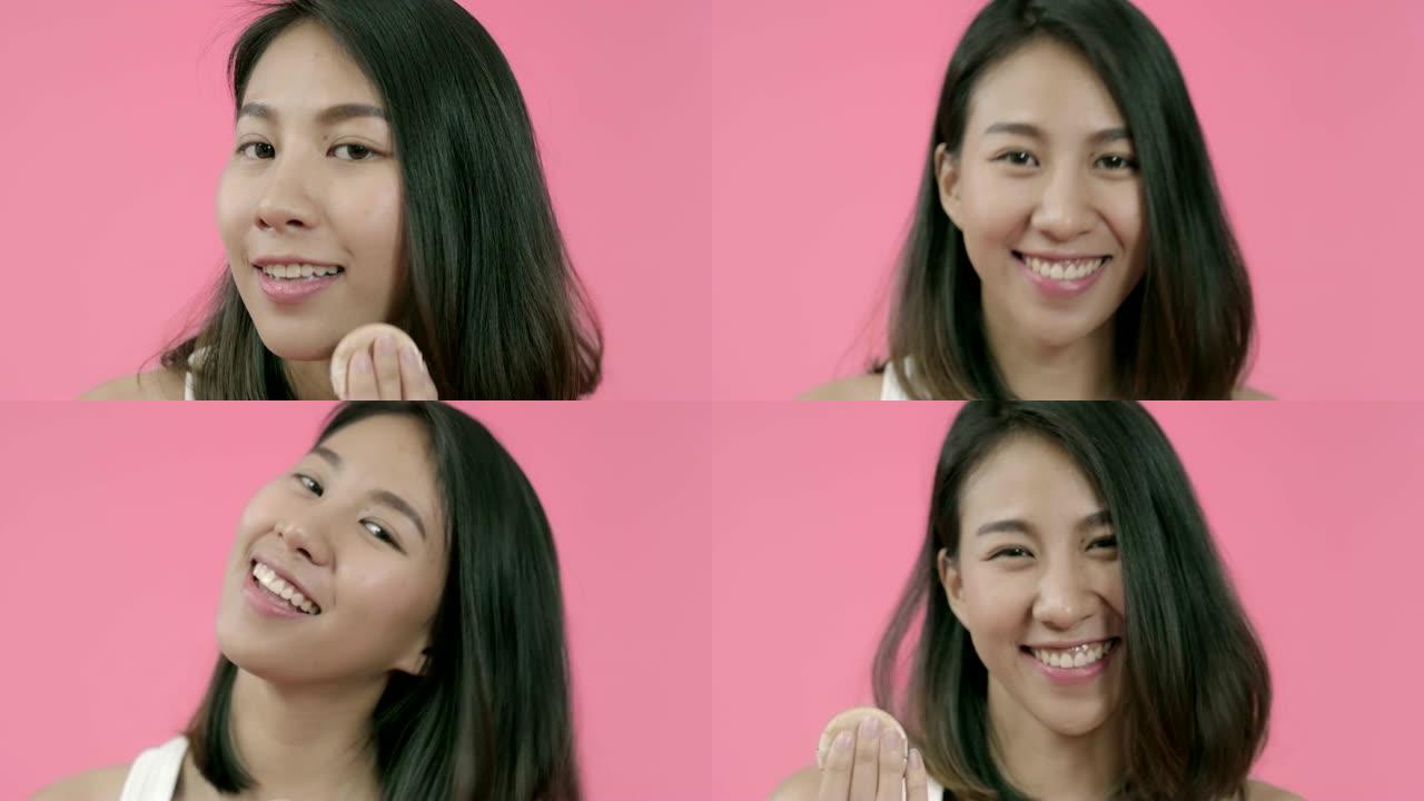 年轻美丽时尚的亚洲女性在粉色背景下用化妆刷在休闲服装上涂抹粉妆。快乐微笑可爱的快乐女人快乐成功。