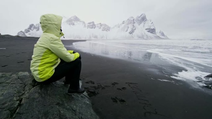 女士坐在冰岛Stokksnes海滩的黑沙滩上