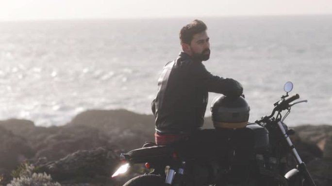 英俊的男人坐在海边的经典摩托车上