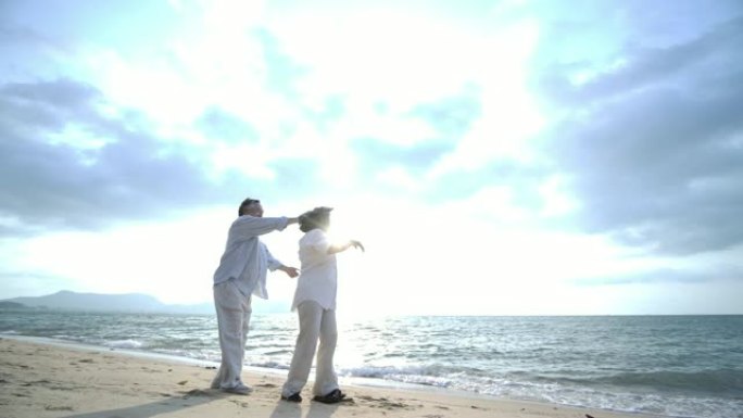 浪漫的亚洲高级夫妇在沙滩上慢动作跳舞。
