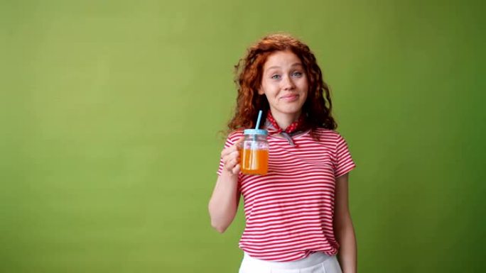 美丽的女孩喝橙汁和绿色背景上的微笑