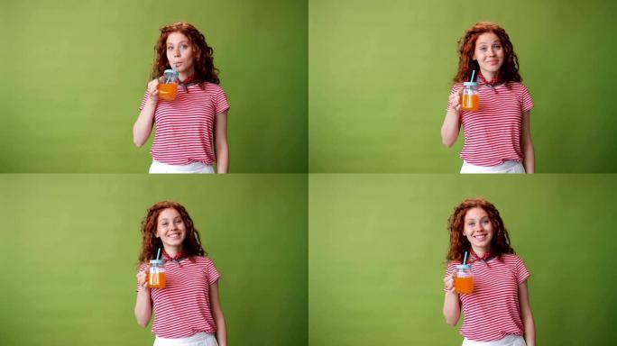 美丽的女孩喝橙汁和绿色背景上的微笑