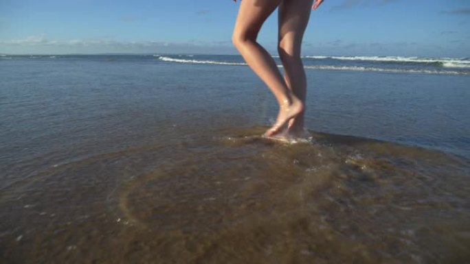 4k慢动作裁剪后视图，显示一名年轻女子的腿沿着南非海滩的水域边缘行走