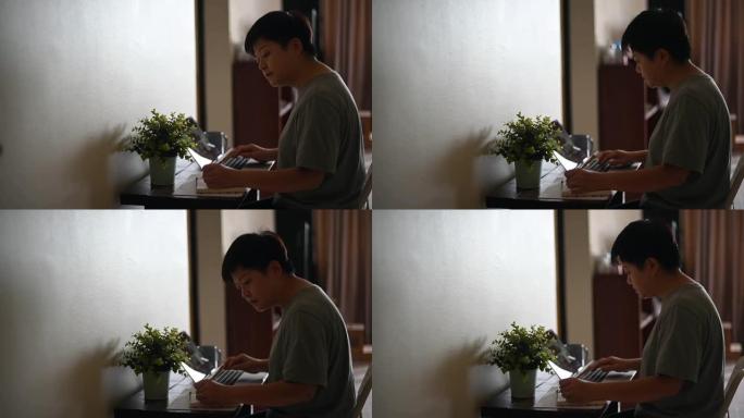 一名在家里工作的亚洲中国女性中年成年人使用她的笔记本电脑和写笔记