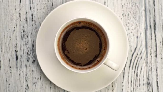 搅拌后，美味可口的热咖啡在白杯中旋转。棕色和橙色，有气泡。自上而下的镜头，4K