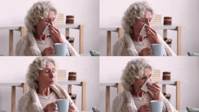 生病的老年妇女覆盖毯子，吹着鼻子在组织中