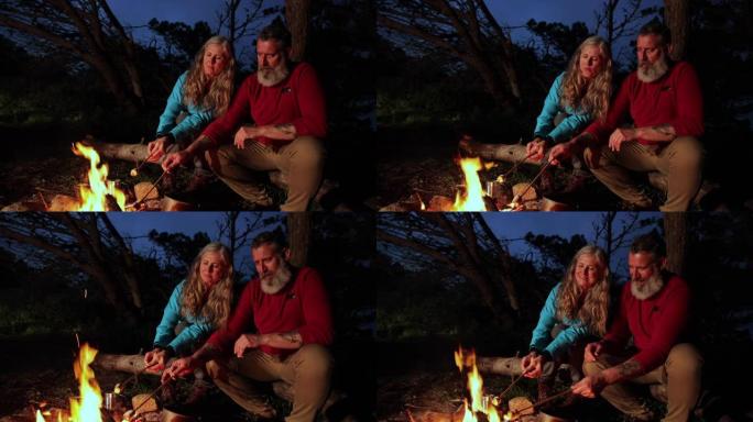 高级夫妇坐在篝火旁煎炸棉花糖