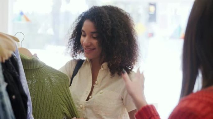 两名年轻女性在时装店的货架上寻找，一起选择套头衫 -- 慢动作拍摄