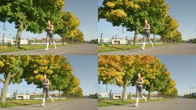 低角度: 微笑的女人喜欢沿着秋天的彩色人行道慢跑。