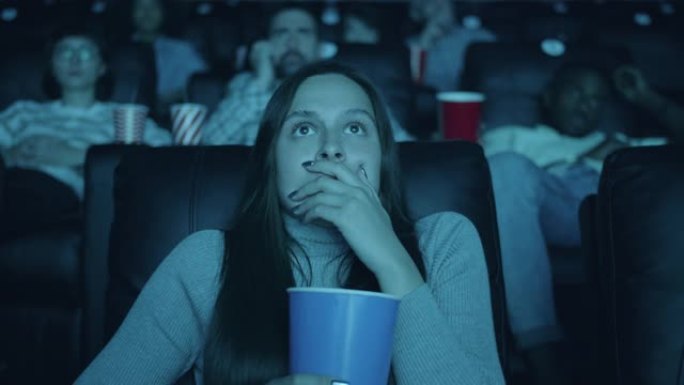 害怕的女人在电影院里张着爆米花看恐怖电影