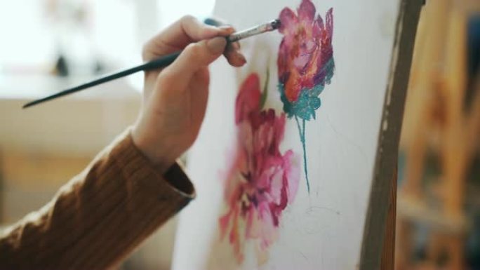 在light studio中，女性手握画笔并在画布上绘制鲜艳花朵的特写镜头。绘画艺术、艺术作品和人民