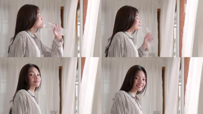 年轻的亚洲迷人的女人在厨房打开窗帘，喝水，早上的时候，微笑，生活方式，自然美丽，在家感觉舒适。