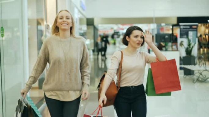 好看的女学生一起走在购物中心，拿着纸袋聊天和大笑。销售、人和购物狂概念。
