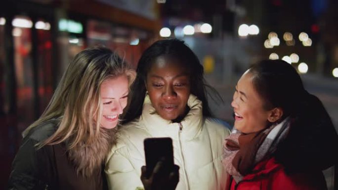 一群晚上在城市街道上的女性朋友使用手机App订购出租车