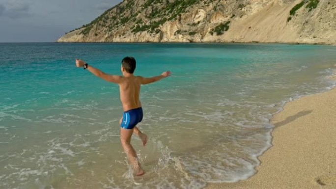 可爱的男孩在海滩上用绿松石水在水中奔跑