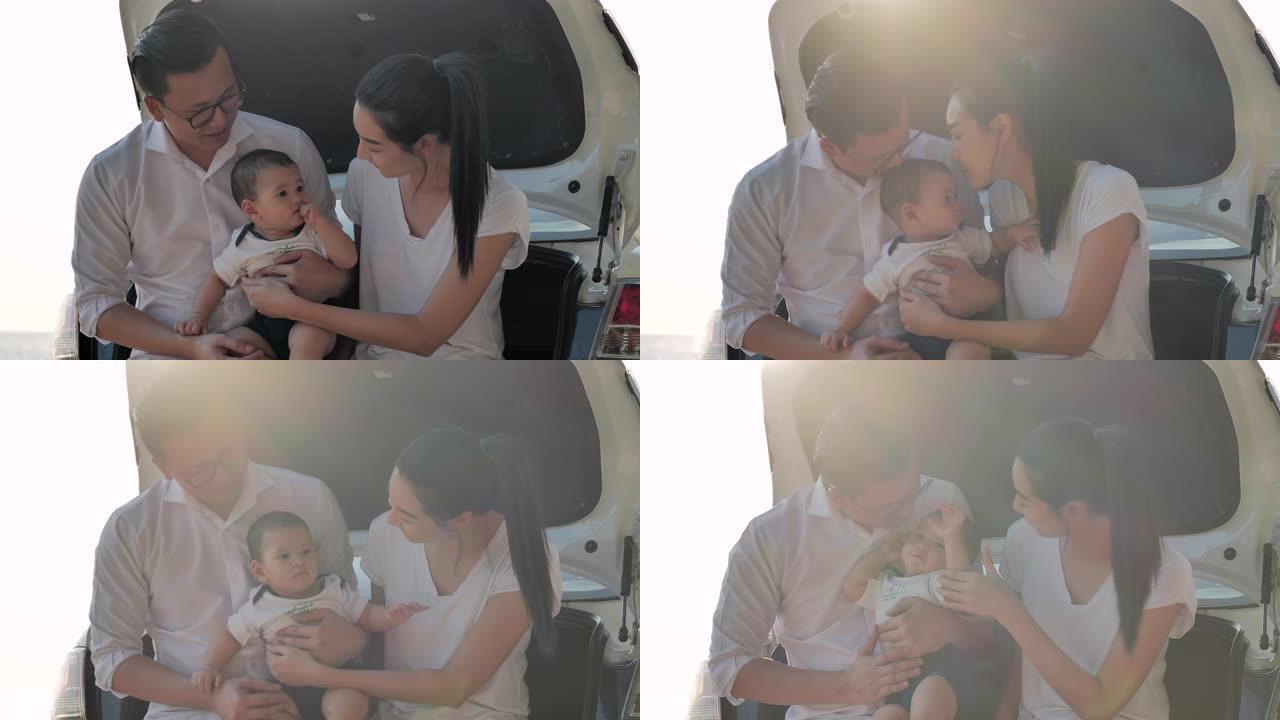 肖像快乐的亚洲家庭亲吻男婴，坐在车里。活跃的父母和人们在暑假与婴儿一起户外活动。快乐的家庭假期。家庭