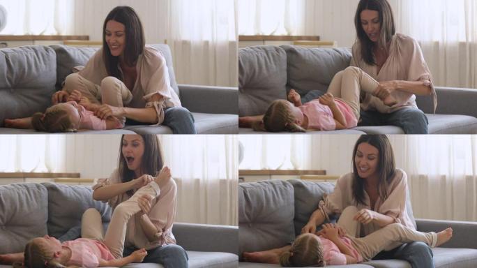 快乐的年轻妈妈和可爱的小女儿在沙发上玩耍