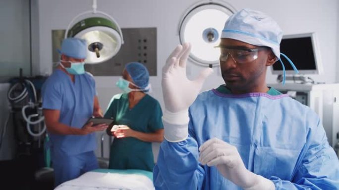 在医院手术室戴着磨砂膏戴上乳胶手套的男性外科医生的肖像