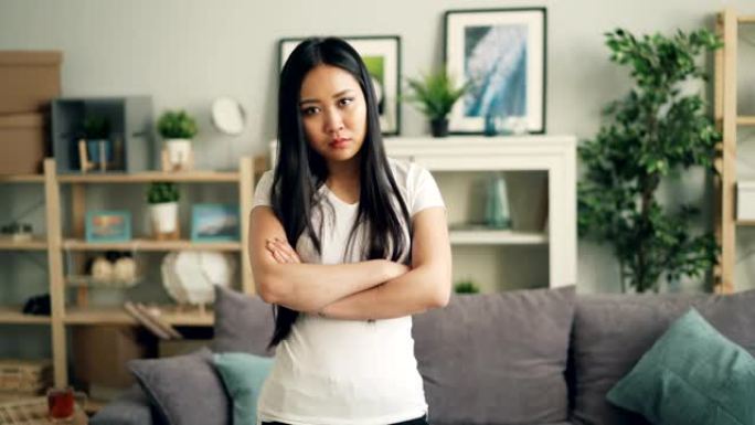 愤怒的亚洲女士的肖像看着相机，皱着眉头，摇摇头表示失望和不赞成，双臂交叉在家里。
