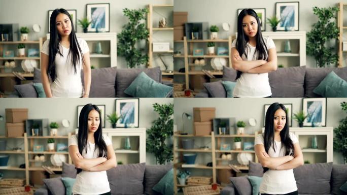 愤怒的亚洲女士的肖像看着相机，皱着眉头，摇摇头表示失望和不赞成，双臂交叉在家里。