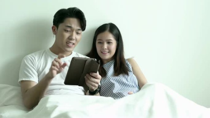 年轻夫妇早上在床上用平板电脑快乐。