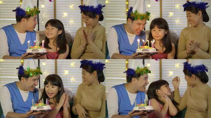 一个可爱的亚洲小女孩用蛋糕和幸福的家庭庆祝她的生日。她露出灿烂的笑容，家人为她鼓掌。慢动作。