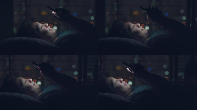 亚洲男子在夜间与bokeh light city一起在床上使用智能手机