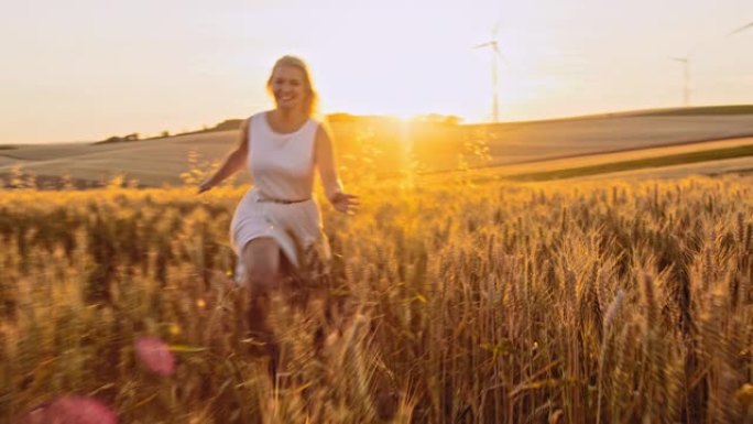 快乐的女人在白色太阳裙跑过一片金黄的麦田在日落