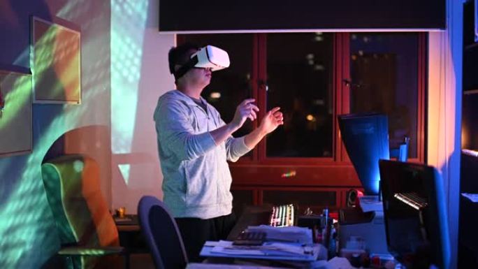 一位亚洲华裔男性晚上在自己的家庭办公室书房里，在台式机前戴上VR护目镜并体验3D虚拟游戏体验