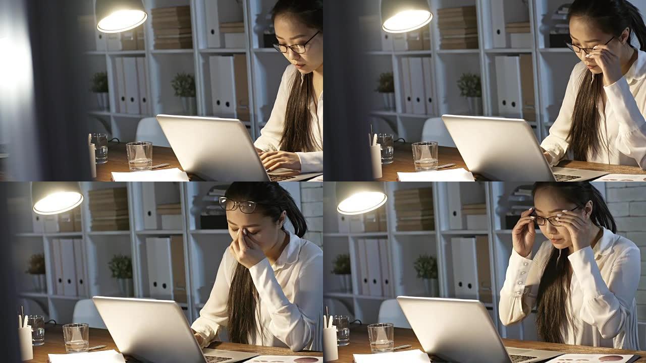 疲惫的亚洲女商人揉眼睛，在笔记本电脑上工作