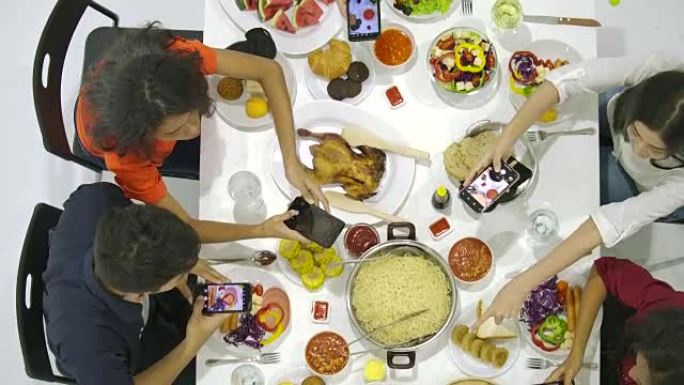 一群朋友在晚宴上与桌子上的所有人一起使用他们的智能手机拍摄晚餐食物的照片。Instagram，社交网