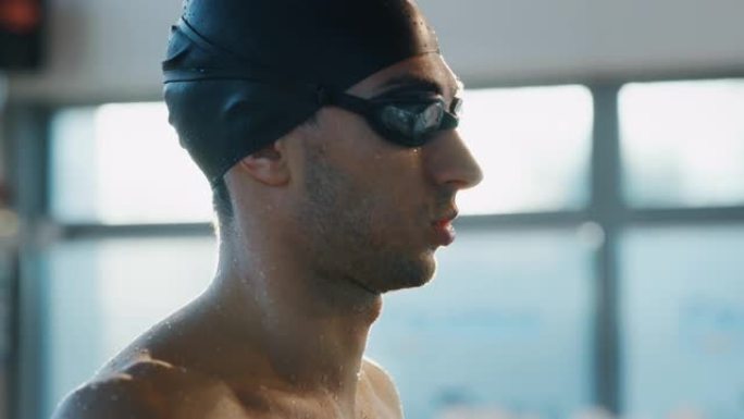 带有谷歌和帽子的微笑专业游泳者的肖像对他在慢动作游泳池中的成绩感到满意。