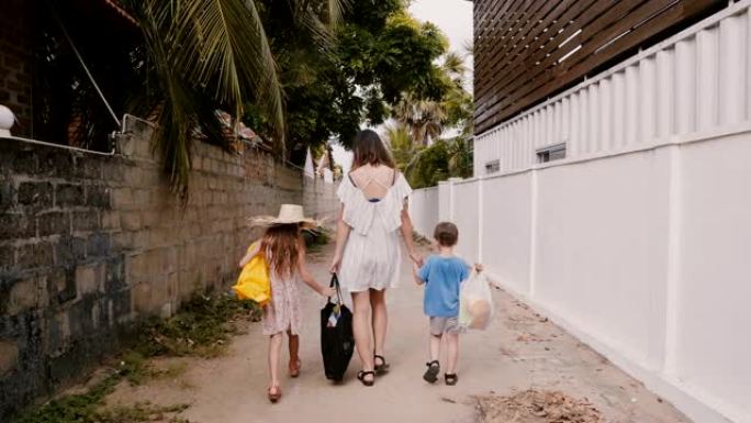 快乐的年轻母亲和两个小孩一起带着购物袋沿着小巷子走向家