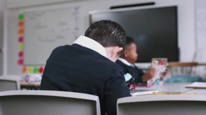 患有唐氏综合症的男孩坐在小学课桌上的背景图，特写