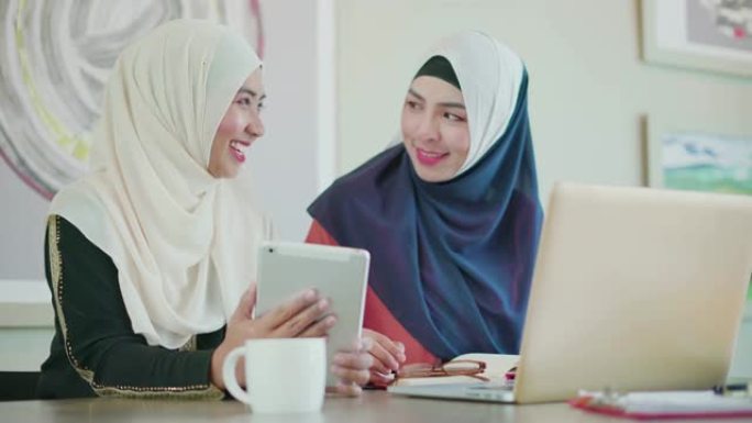 两个穆斯林人在工作场所使用平板电脑和笔记本电脑进行工作和讨论。