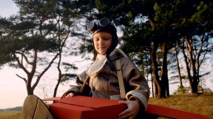 正面的小飞行员男孩在树下穿着有趣的纸板飞机服装，穿着复古飞行员超级英雄眼镜慢动作